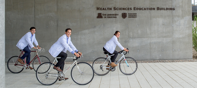 three medical students riding bicycles on the medical school campus