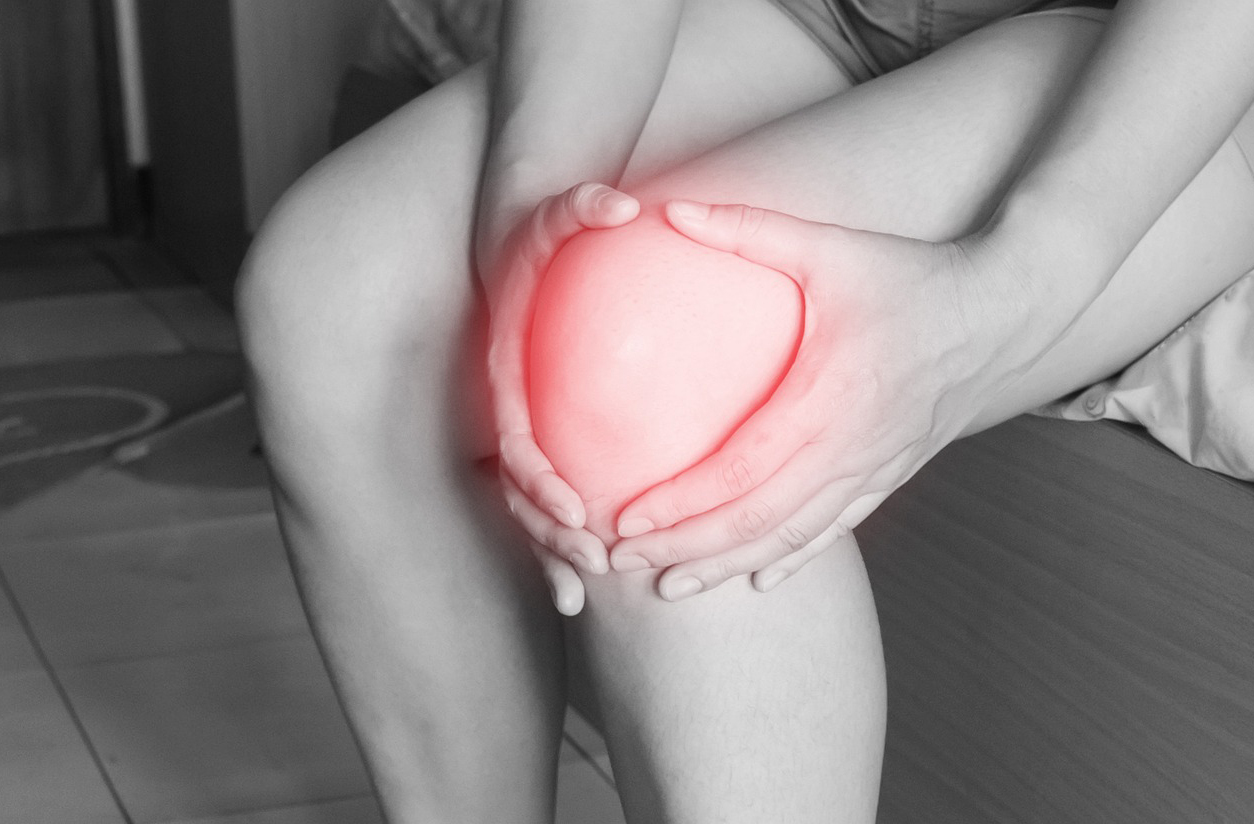 A woman holds her injured knee, which is highlighted red to note injury