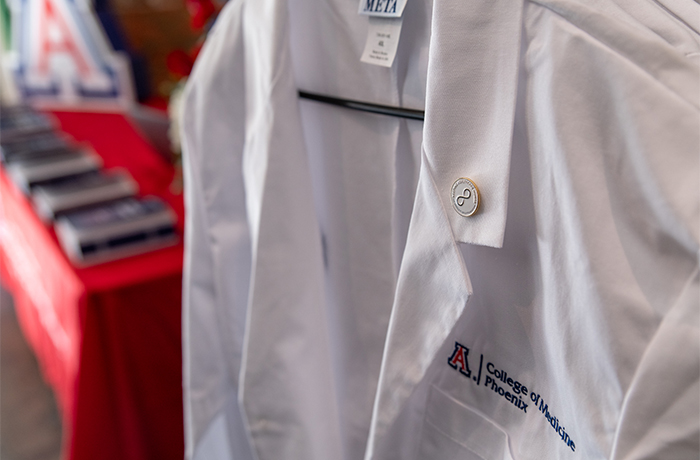 A White Coat hangs on a hanger with textbooks in the background