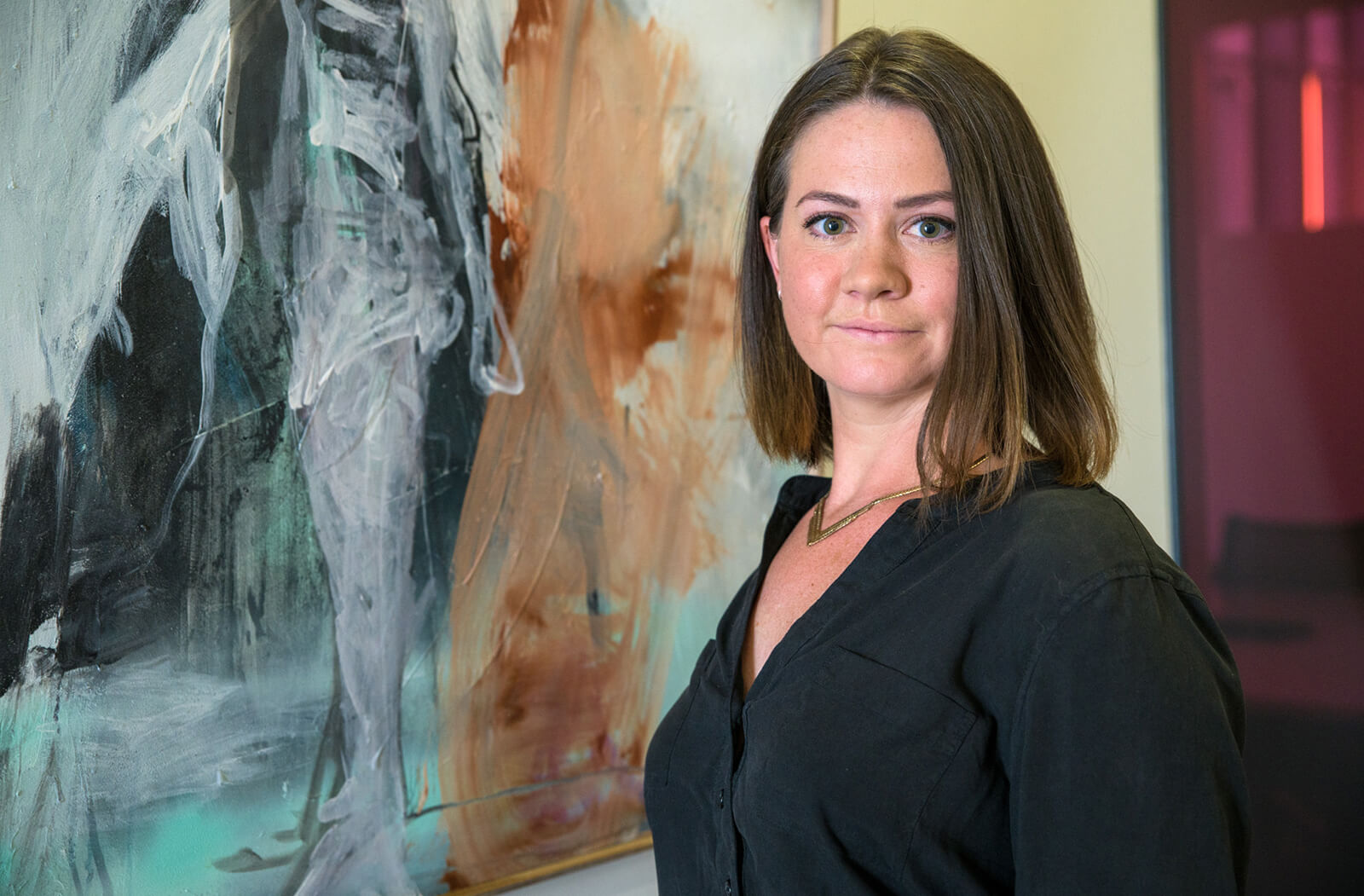 Harriet Barratt, MD, poses in front of one of her paintings on the fifth floor of the Health Sciences Education Building