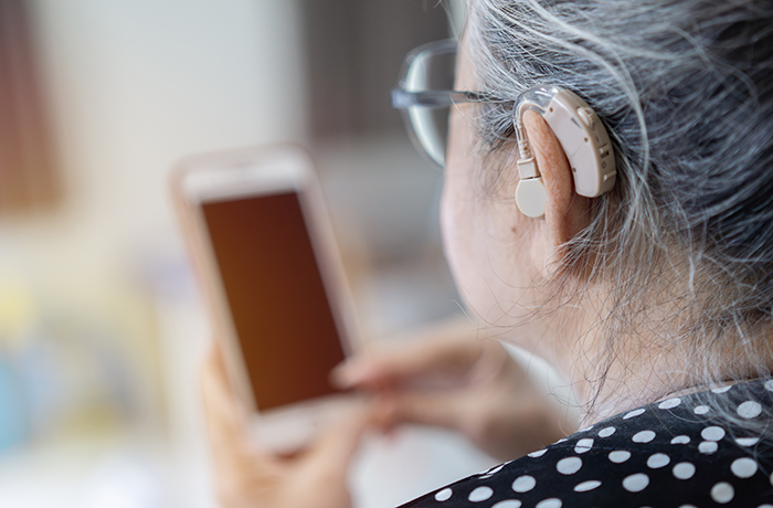 An elderly woman wearing a hearing aid looks at her phone