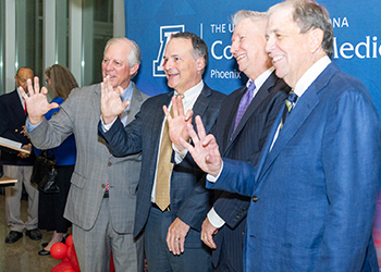 Image of four male in suits waving their hands at a university reception