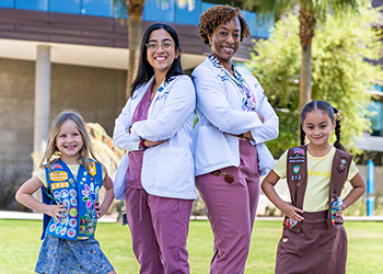 Image of two young Girl Scouts in uniform standing with two female medical students in white coats