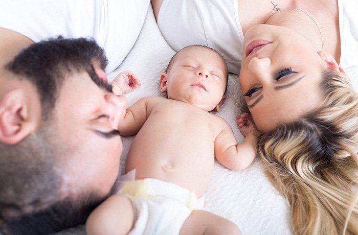 A dad, baby and mom in laying in bed