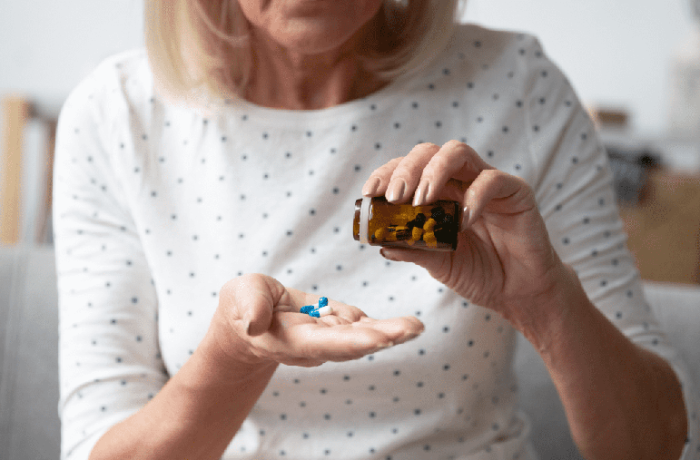 An older woman pours pills into her hand