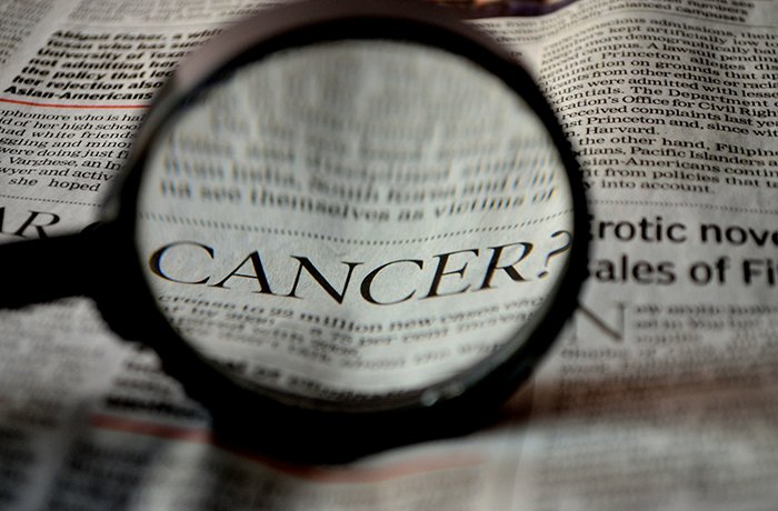 A magnifying glass zooms in on the word "Cancer"