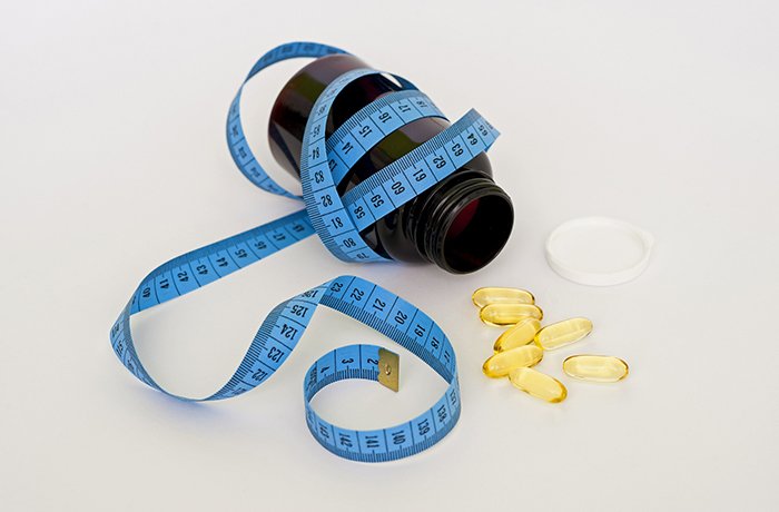 A waist measurer is wrapped around an open bottle of pills