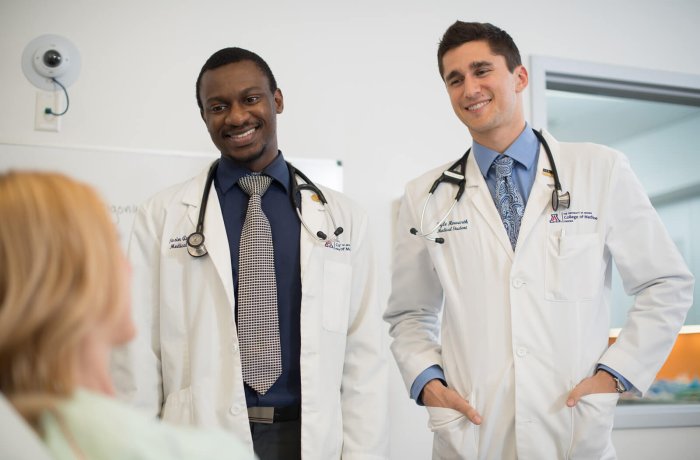 Two medical students talk to a mock patient