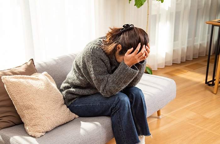 A woman sits alone on her couch with her head in her hands