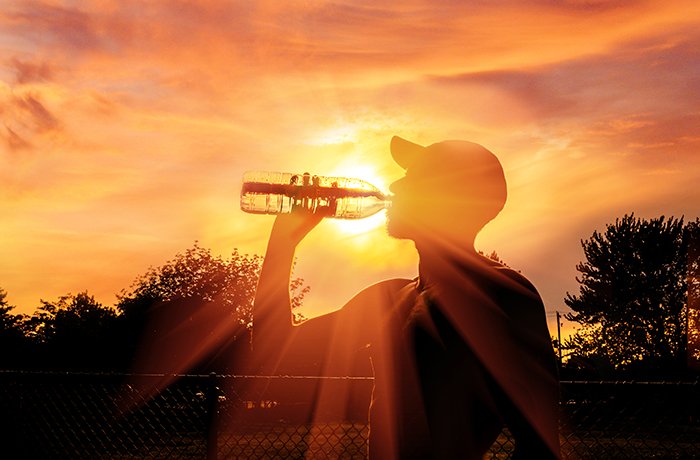 A man drinks water outside in the sun