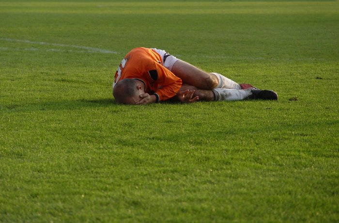 Soccer player lying on the ground in pain, holding his head, during a match on a green field