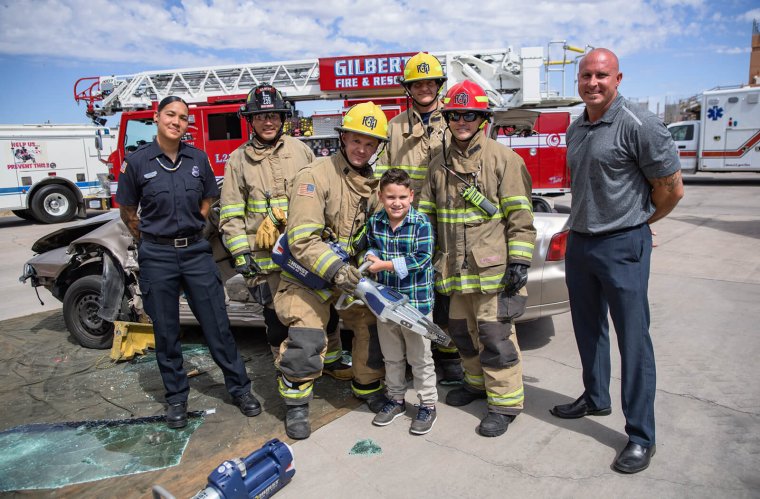 Simulated crash training crews with Glendale Fire paramedic Alex Matthews (left), her son, Jamison (holding jaws-of-life device), and Mesa and Gilbert Fire crews. Alex and Jamison were in a motor vehicle accident in December 2012, where Alex used the EPIC-TBI prehospital care guidelines to help save the life of her son. Simulated crash training crews with Glendale Fire paramedic Alex Matthews (left), her son, Jamison (holding jaws-of-life device), and Mesa and Gilbert Fire crews. Alex and Jamison were in a motor vehicle accident in December 2012, where Alex used the EPIC-TBI prehospital care guidelines to help save the life of her son.