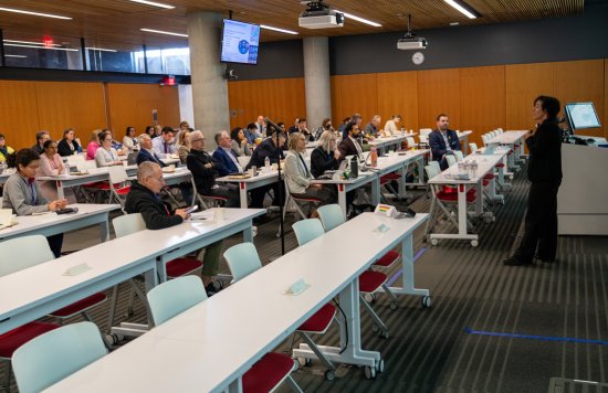 A conference room filled with attendees listening to a speaker.
